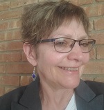 white woman with short hair, big earrings, and glasses.
